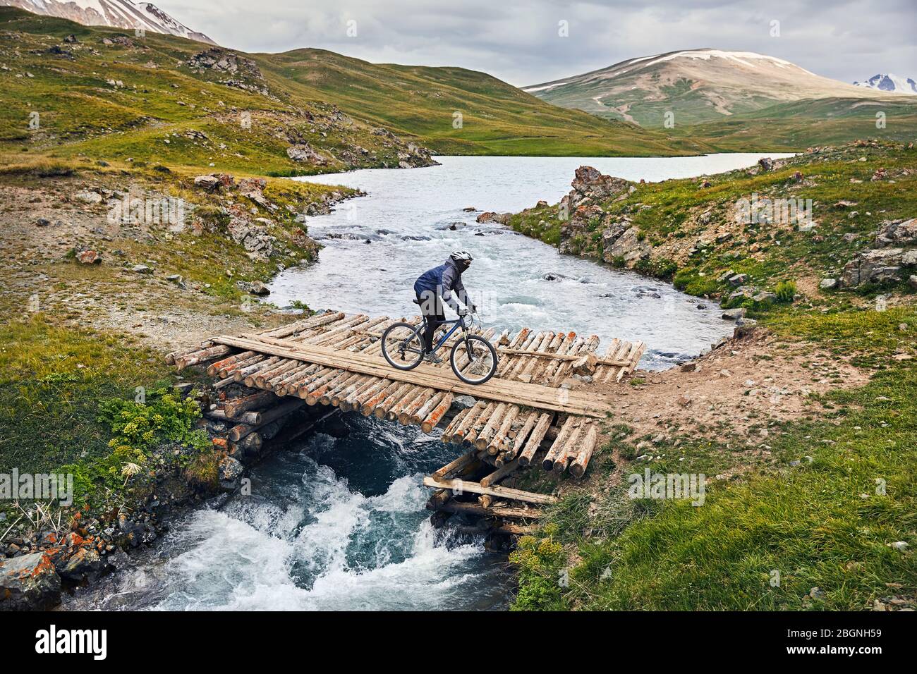 Man on mountain bike crossing the river by wooden bridge in the