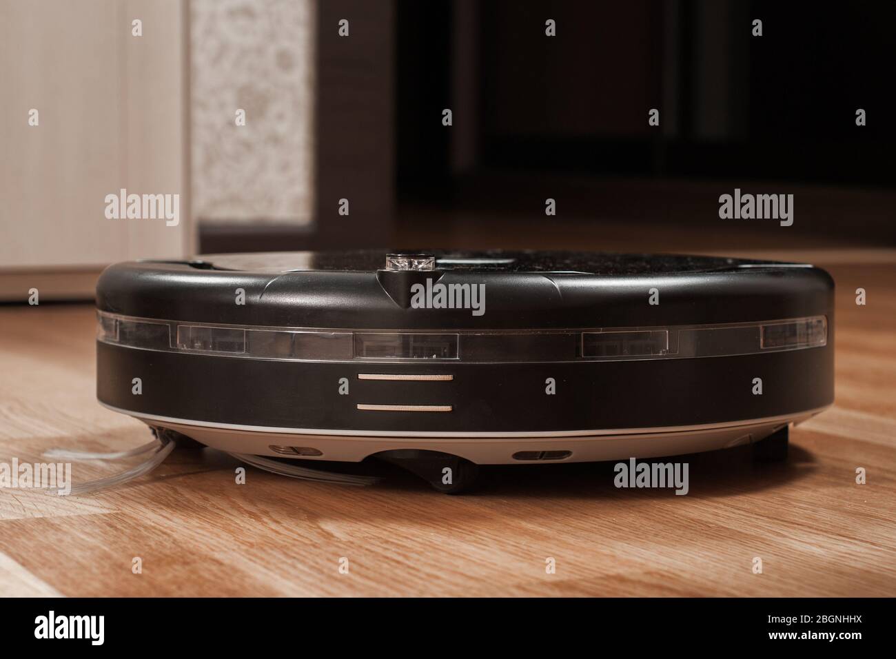 black robotic vacuum cleaner running on laminate floor in bedroom