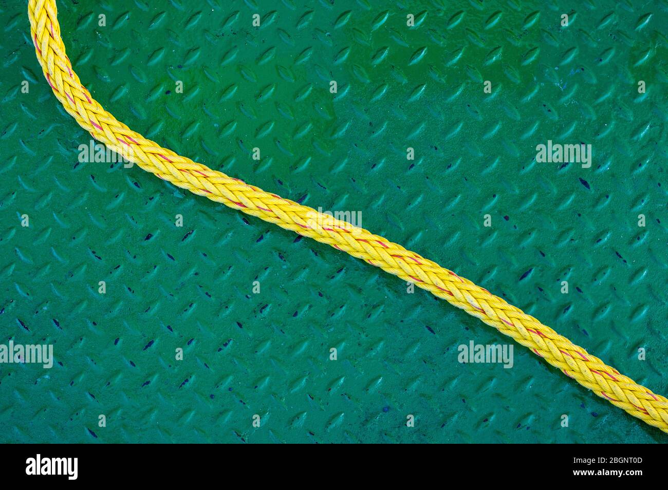 yellow, braided boat line lies loosely on green, worn checker plate from top left in the s-curve to the bottom right Stock Photo