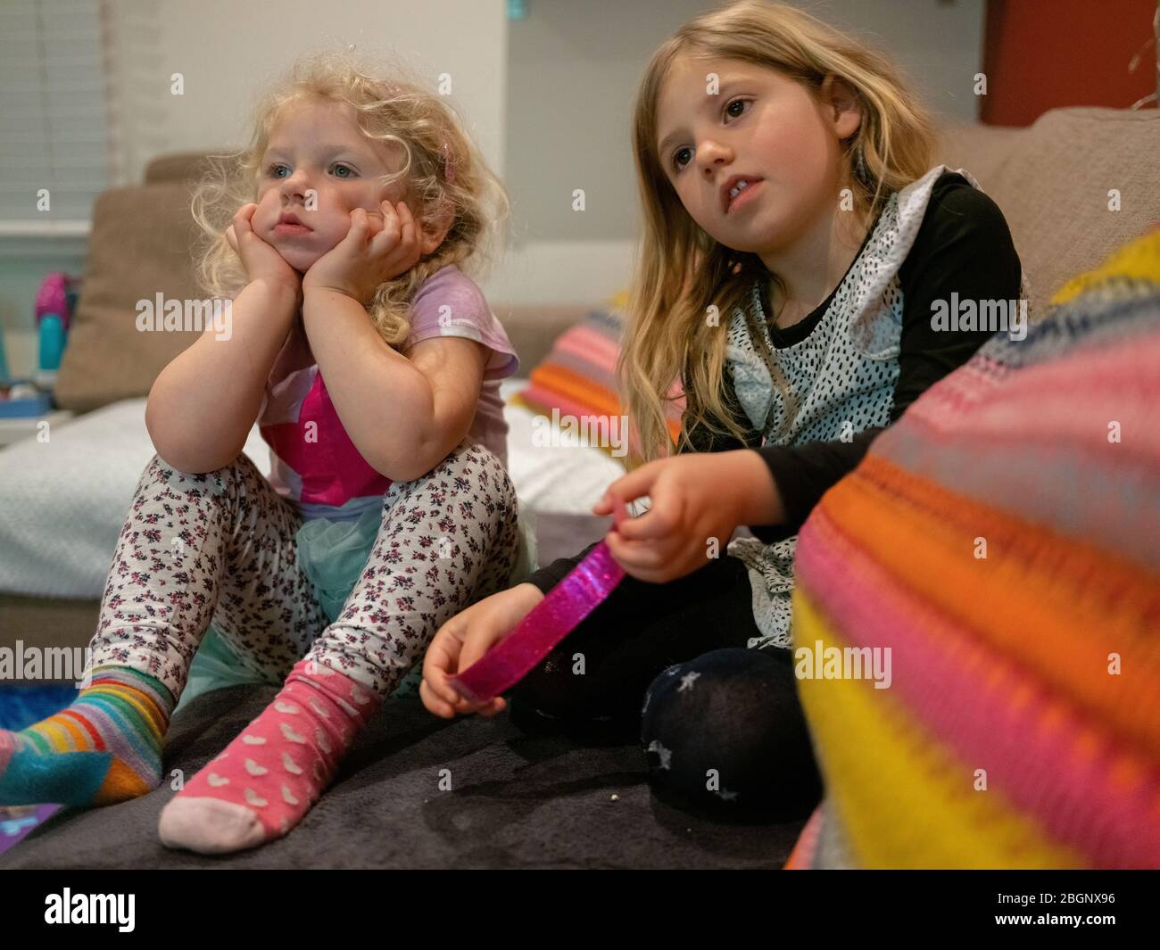 3rd April 2020 Two young sisters bored at home watching television. They are 4 and 2 years old. Taken during the coronavirus lockdown.  London, UK Stock Photo