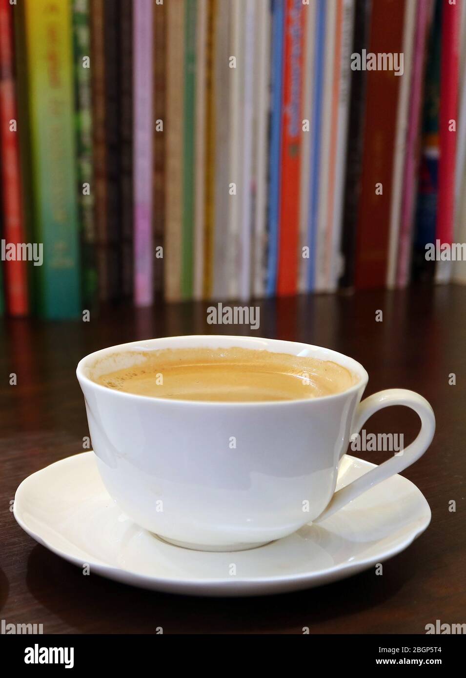 Vertical Image of a Cup of Hot Coffee with Blurry Book Shelf in Background Stock Photo