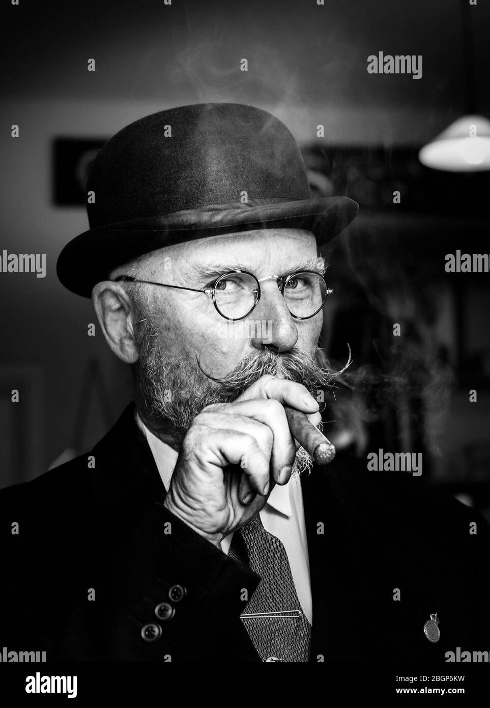 Monochrome front close-up portrait of 1940s British man with handlebar moustache & bowler hat smoking cigar, 1940s UK summer event. Stock Photo