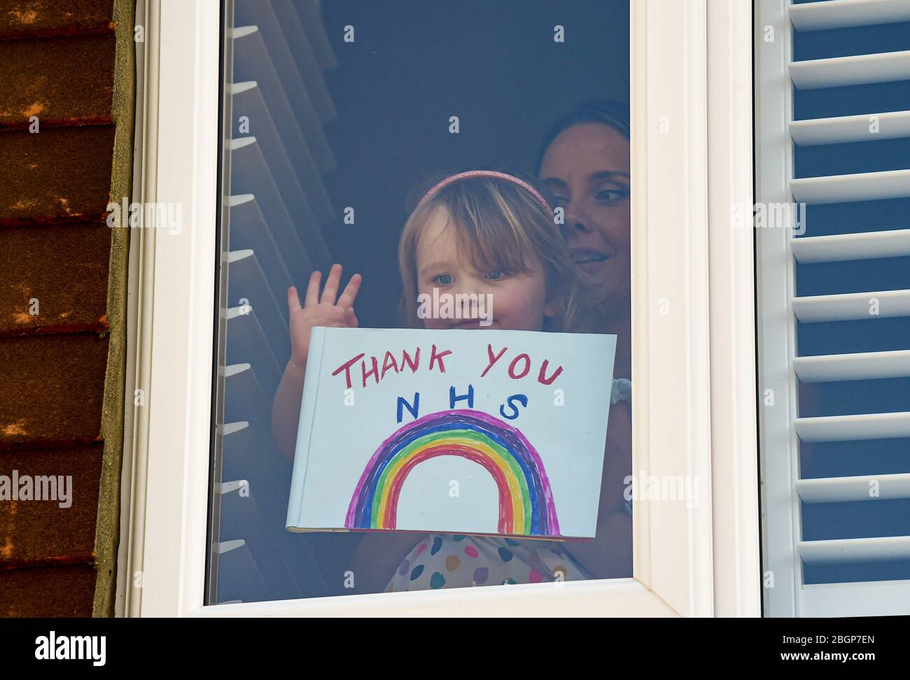 Brighton UK 22nd April 2020 - A young girl and her mother stick a Thank You NHS rainbow painting and message to their Woodingdean house window near Brighton during lockdown in the Coronavirus COVID-19 pandemic crisis  . Credit: Simon Dack / Alamy Live News Stock Photo