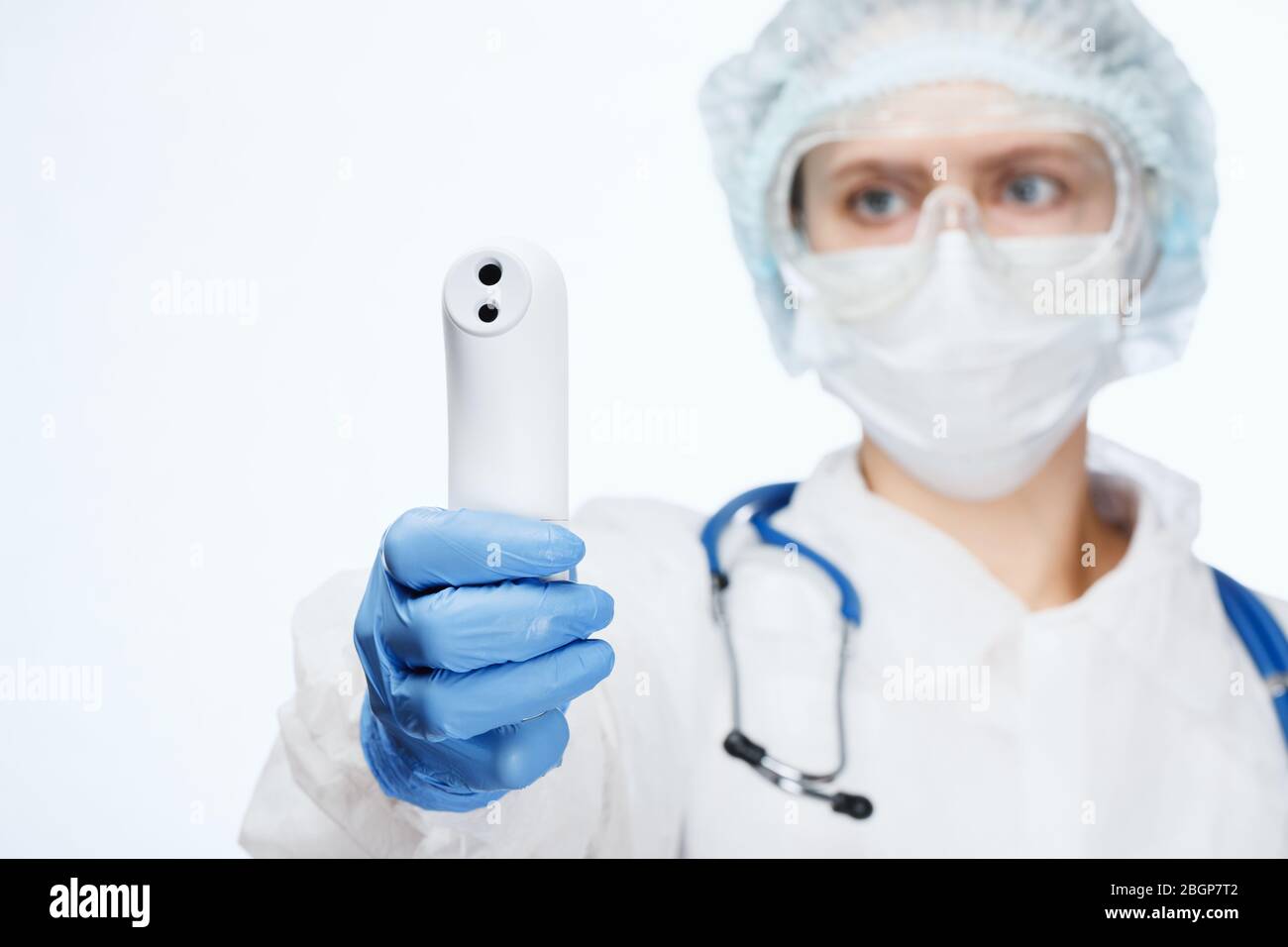 Close-up shot of doctor wearing protective suit and surgical mask using infrared forehead thermometer or thermometer gun to check body temperature for Stock Photo