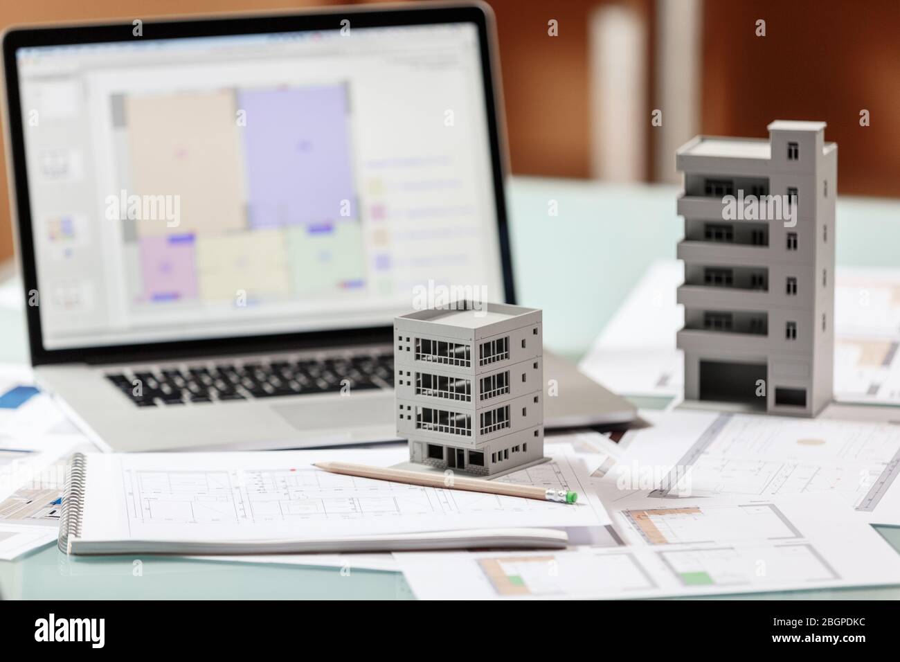 Close up of a house model standing over apartment plans in front of a laptop in a construction bureau. Architectural and construction bureau working c Stock Photo