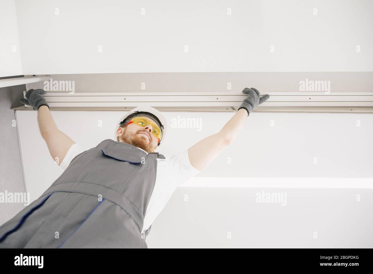 Male builder carpenter installs curtain on ceiling, bottom view Stock Photo