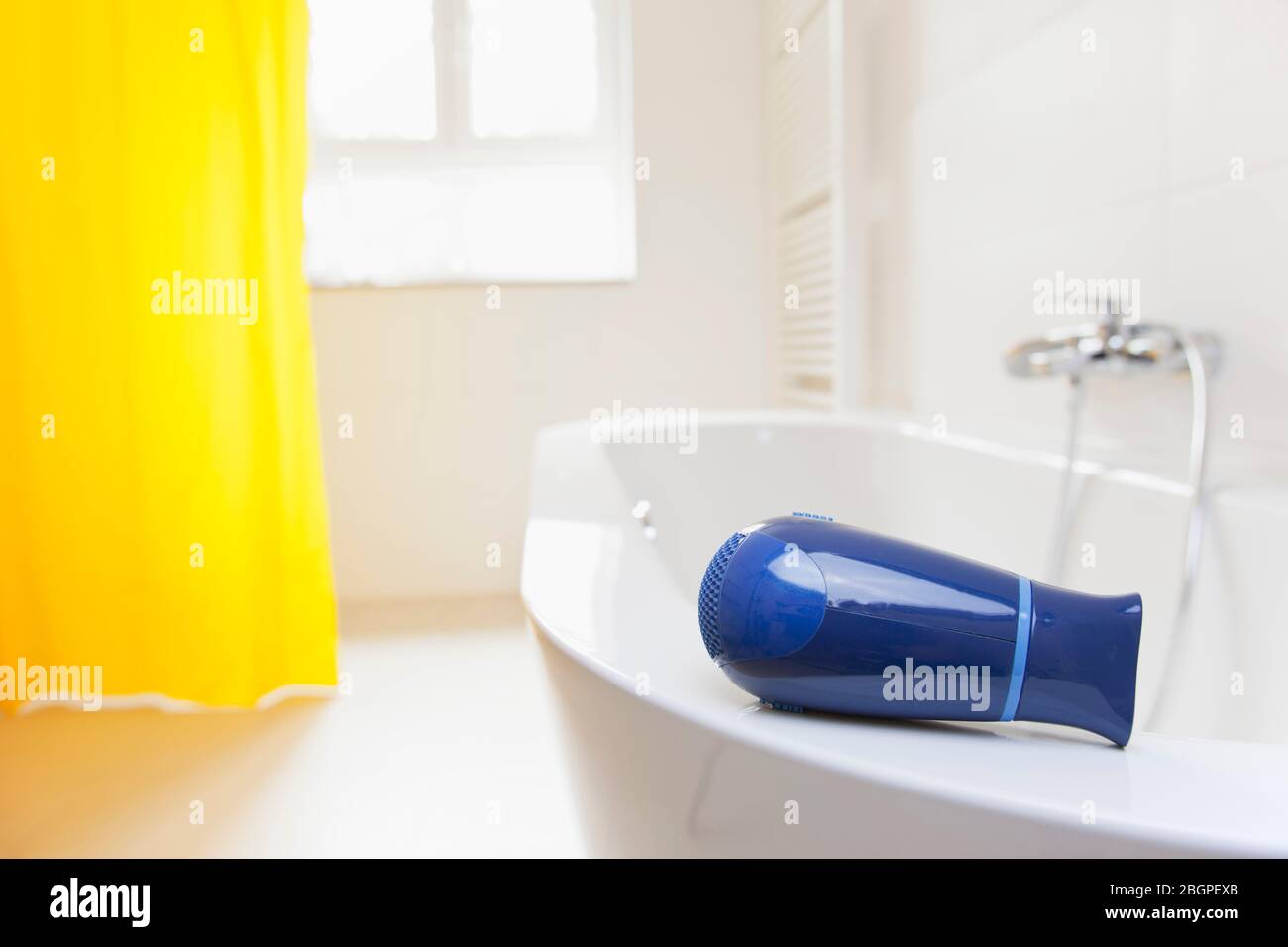 Hair dryer lying on a bathtub in a bright bathroom - danger of electric shock - selective focus on the hair dryer Stock Photo