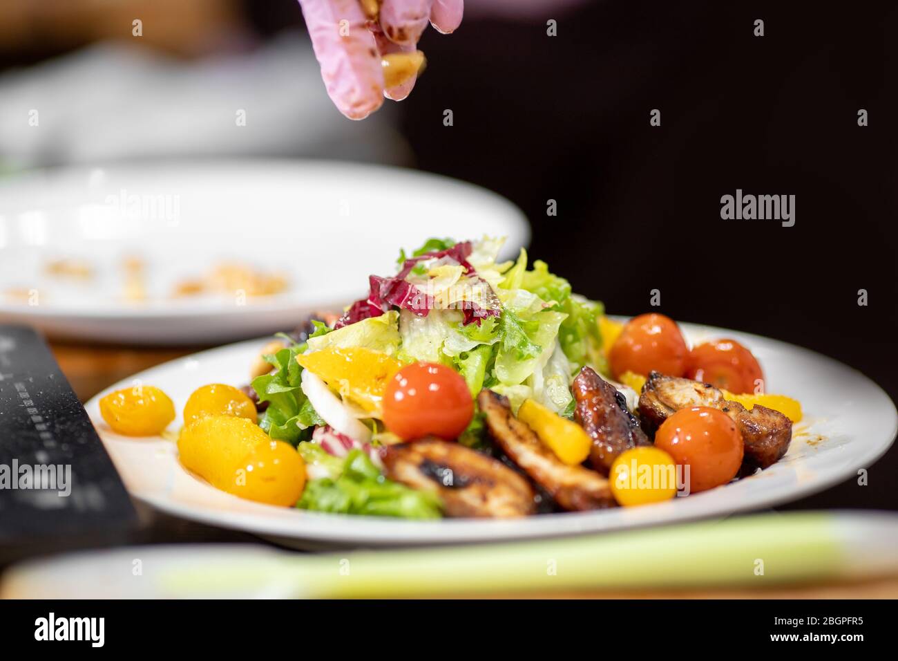 Juicy healthy salad with fried chicken, tomatoes, herbs, oranges, almonds on white plate Stock Photo