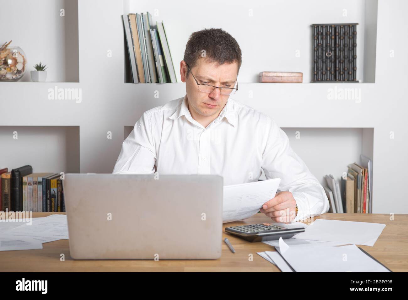 Businessman receiving negative news, touching his glasses, being mad, upset and surprised in front of laptop. Stock Photo