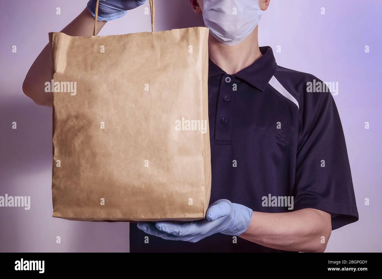 Safe food delivery. A courier in a protective mask and gloves delivers food, parcels and goods during quarantine of the coronavirus. With copy space. Stock Photo