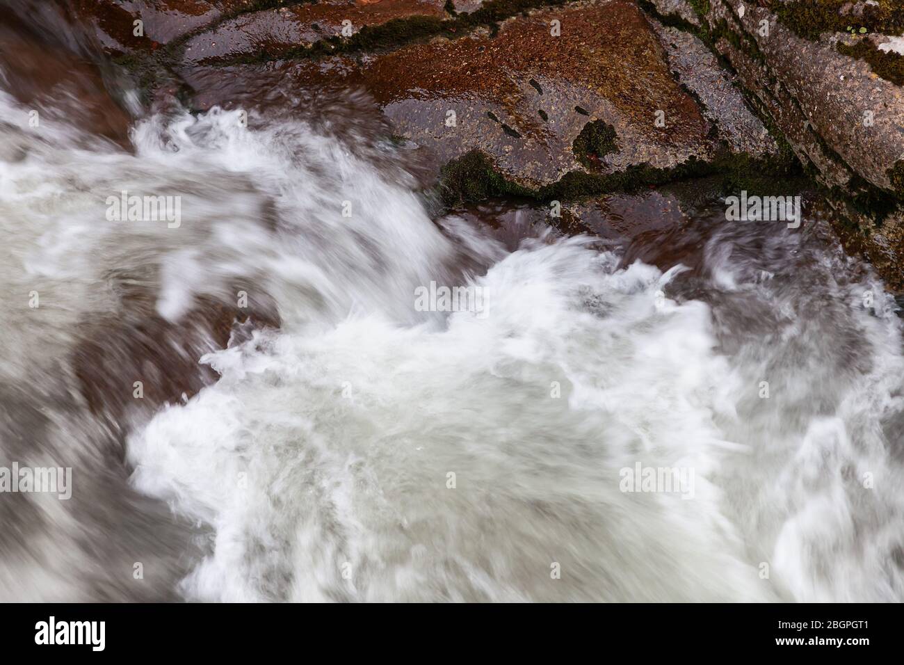 Beautiful close up details and shapes of powerful mountain creek rapids cascading over red, wet rocks of a canyon Stock Photo