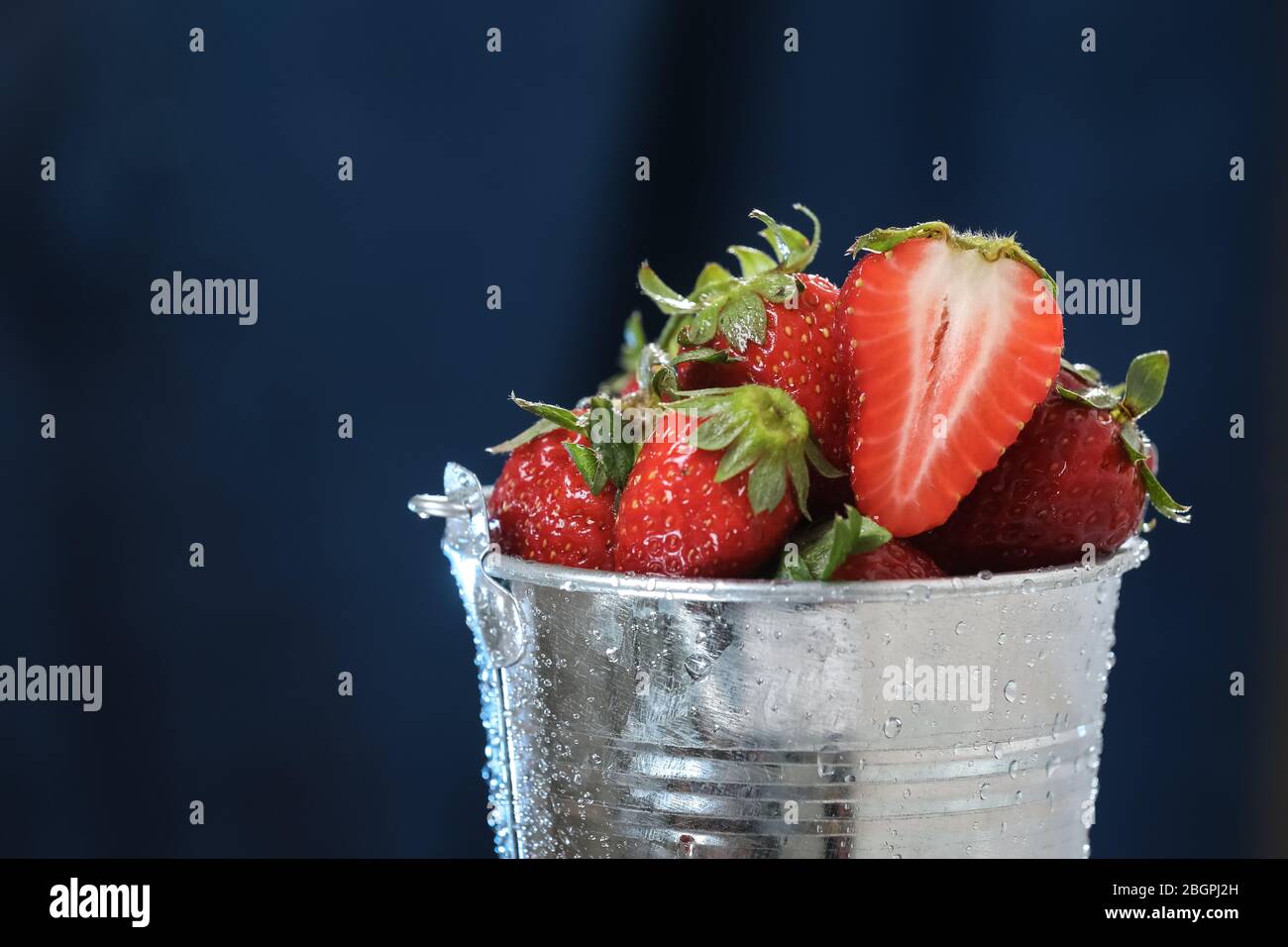 Red strawberries in a metal bucket closeup in a blue background ...