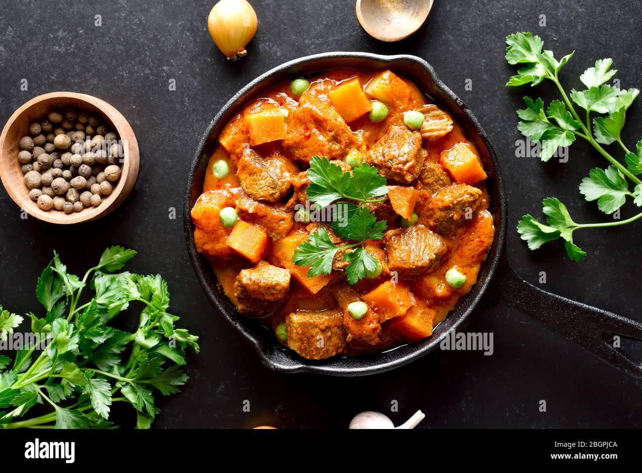 Beef stew with potatoes and carrots in tomato sauce on black background