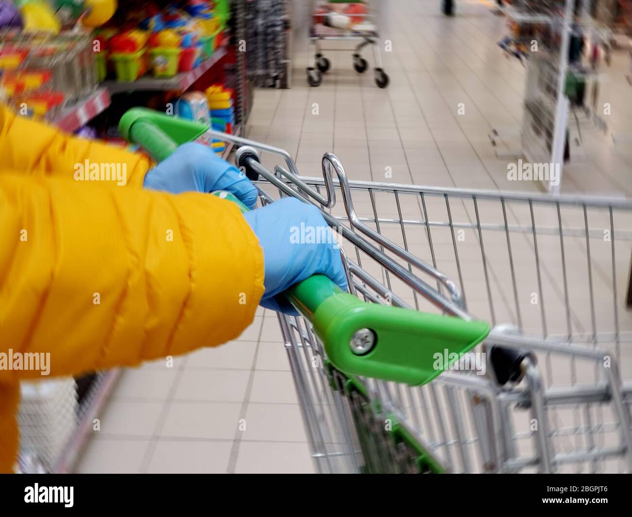 Womans hands in medical protective glove gloves hold the handle of the grocery cart, close-up. Coronavirus protection in the supermarket Stock Photo