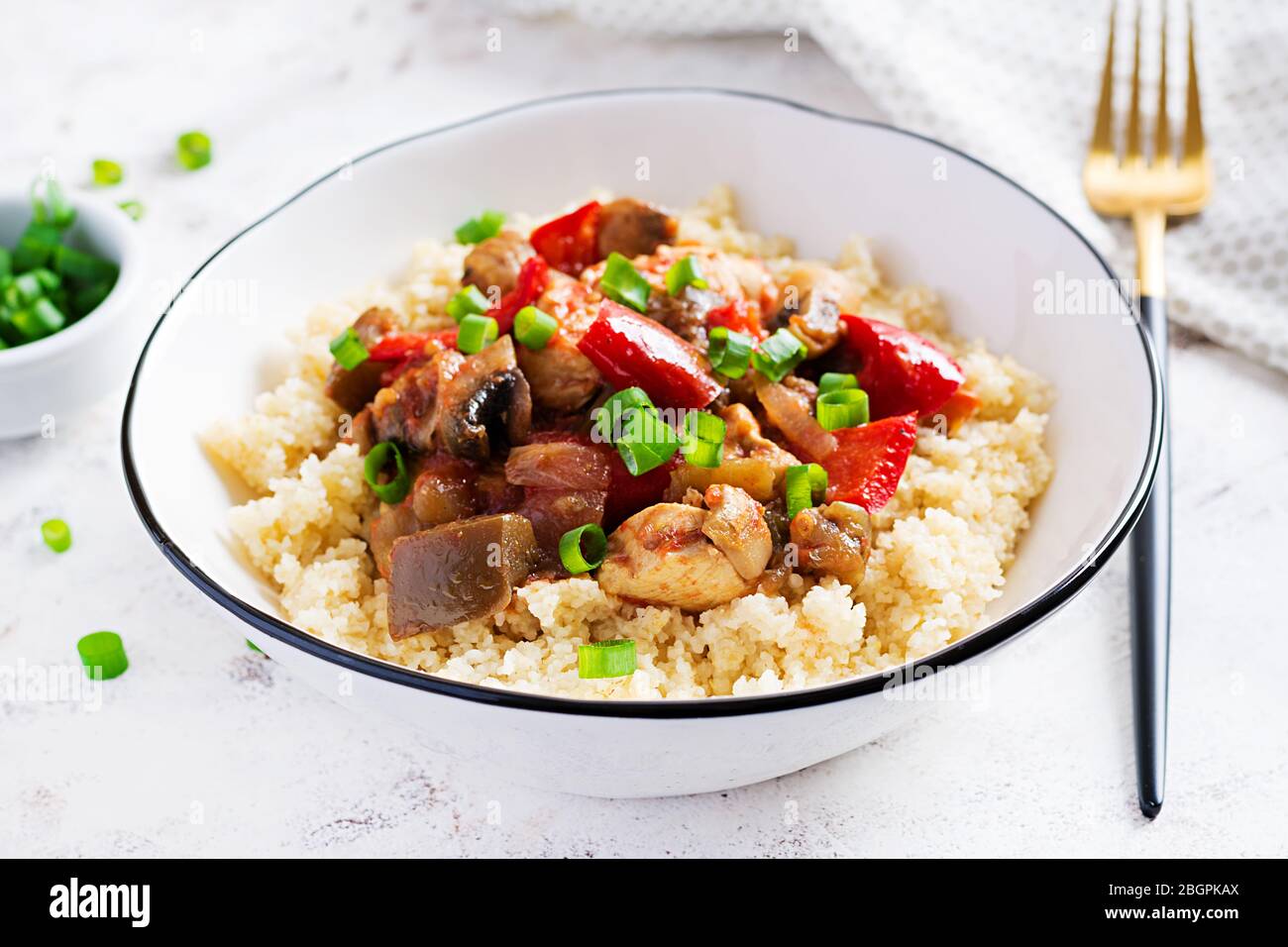 Bulgur and sauteed chicken, mushrooms, eggplants, paprika and tomatoes in a white bowl Stock