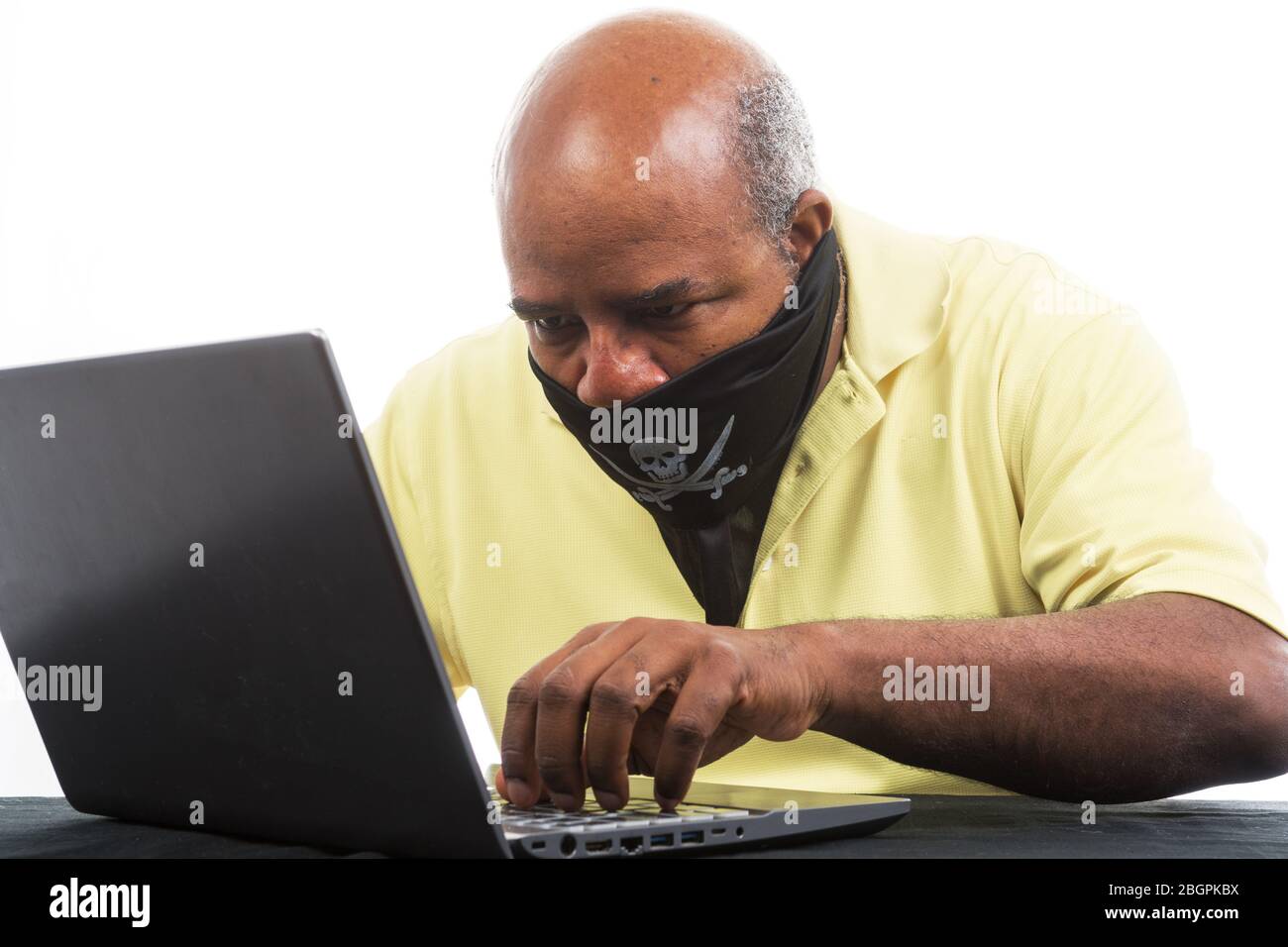 African American Man is hacking a laptop computer waering a pirat mask. Stock Photo