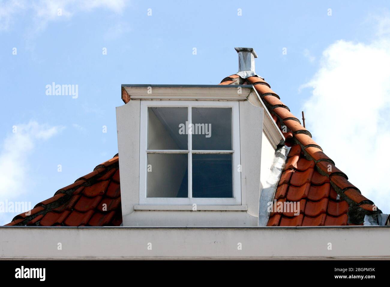 A skylight on red tiled roof, blue sky in the backgroundEin Dachfenster auf rotem Ziegeldach, blauer Himmel im Hintergrund Stock Photo