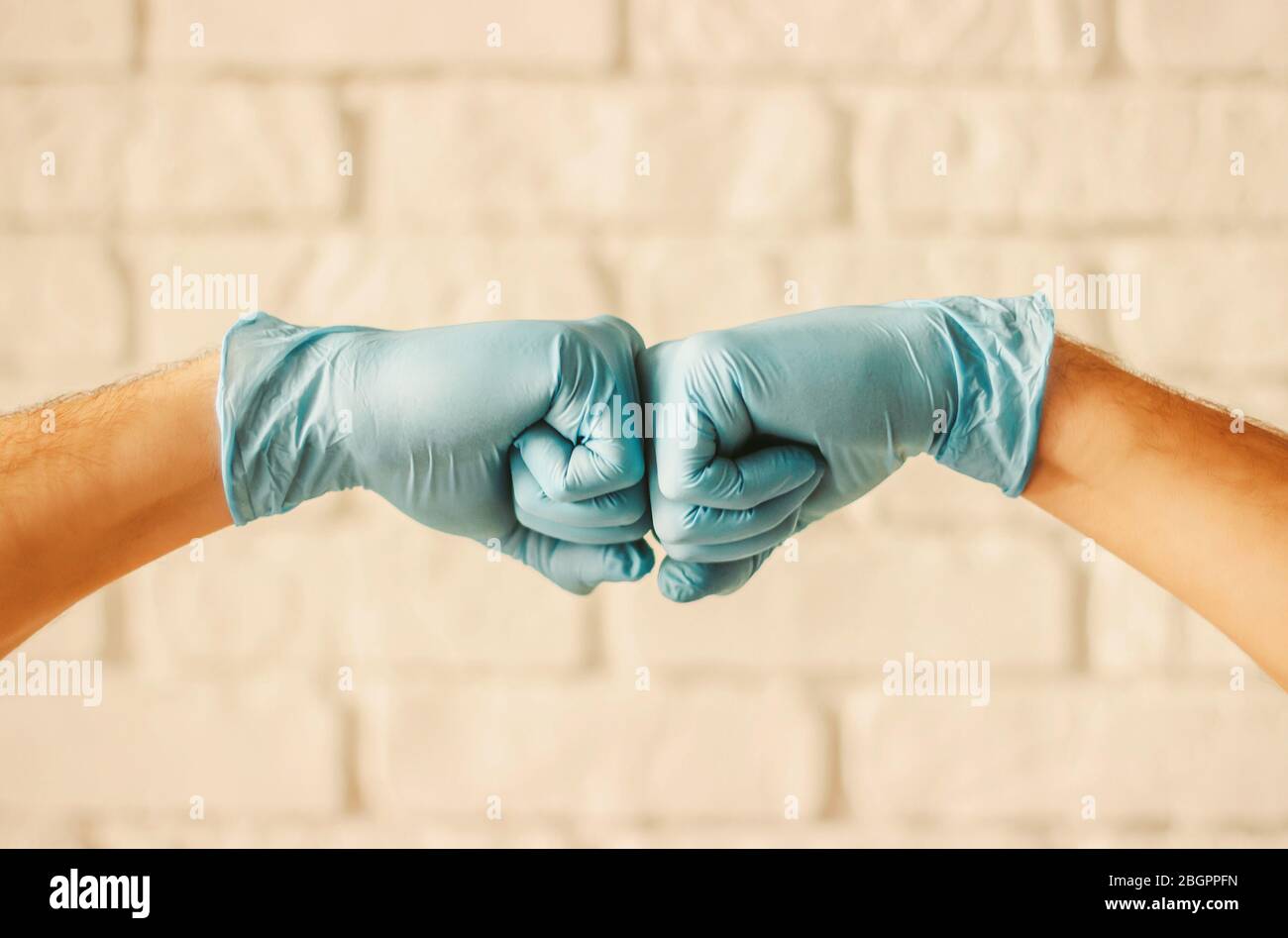 Two men bumping hands in blue medical gloves as protection against coronavirus. Doctor surgeons in blue protective latex gloves clapping fists. COVID- Stock Photo