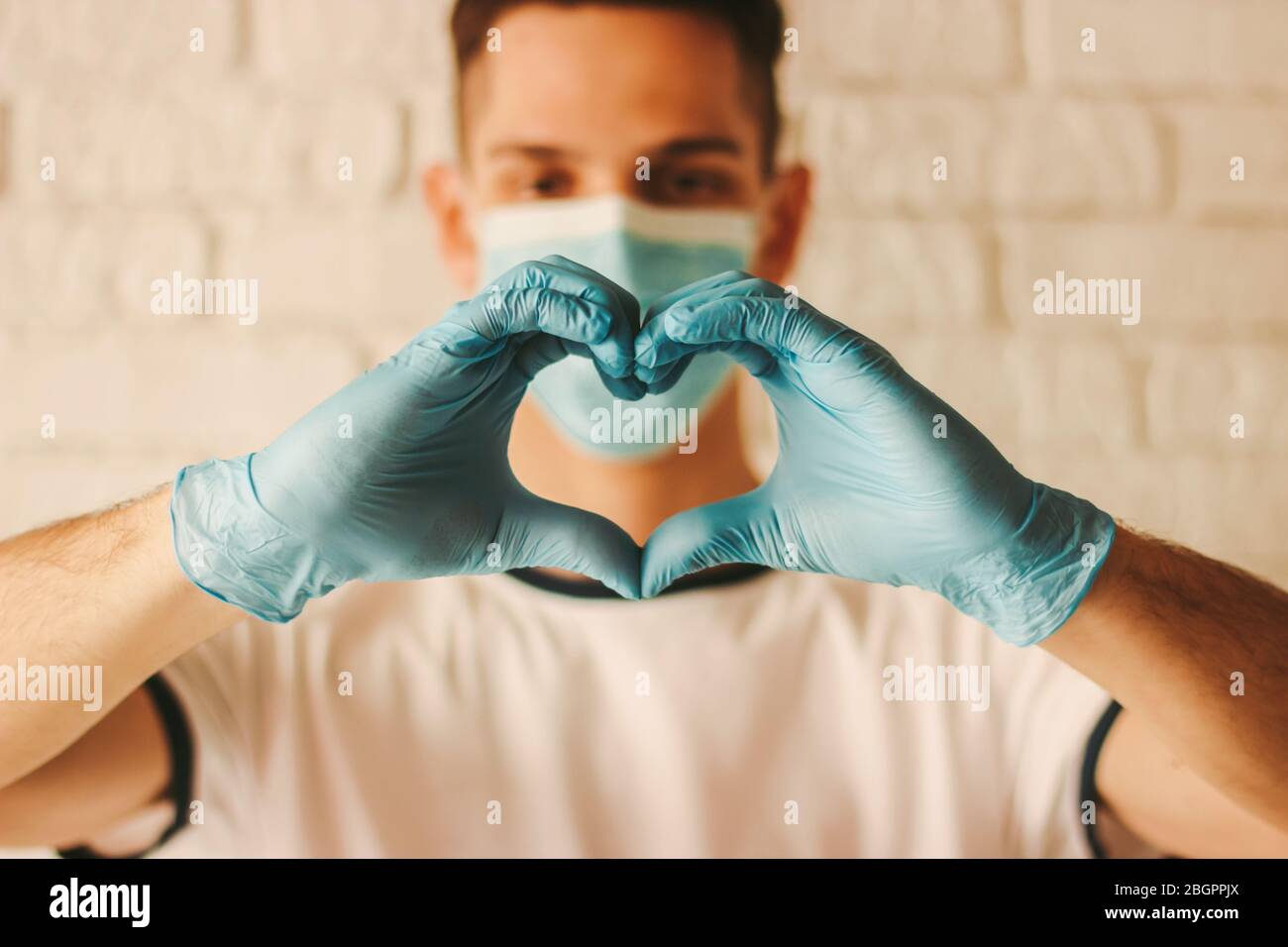 Doctor in protective face mask and medical gloves on hands showing love symbol. Young man in medical face mask and protective gloves gesturing heart s Stock Photo