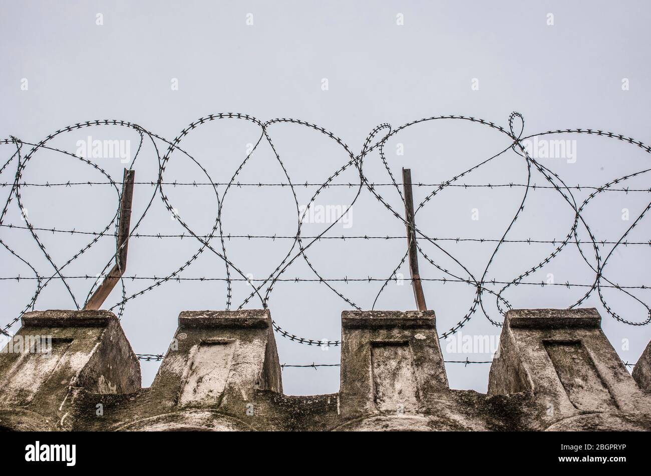 Concertina wire placed on the top of a wall. Grey cloudy sky Stock Photo