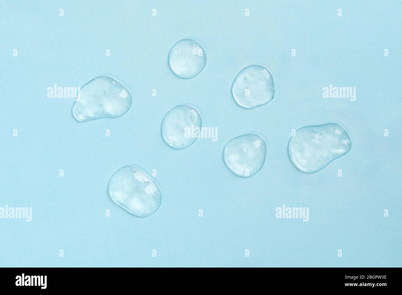 Squeezed cosmetic clear cream gel texture. Close up photo of transparent drop of skin care product. High Quality transparent gel with bubbles closeup on blue background. Stock Photo