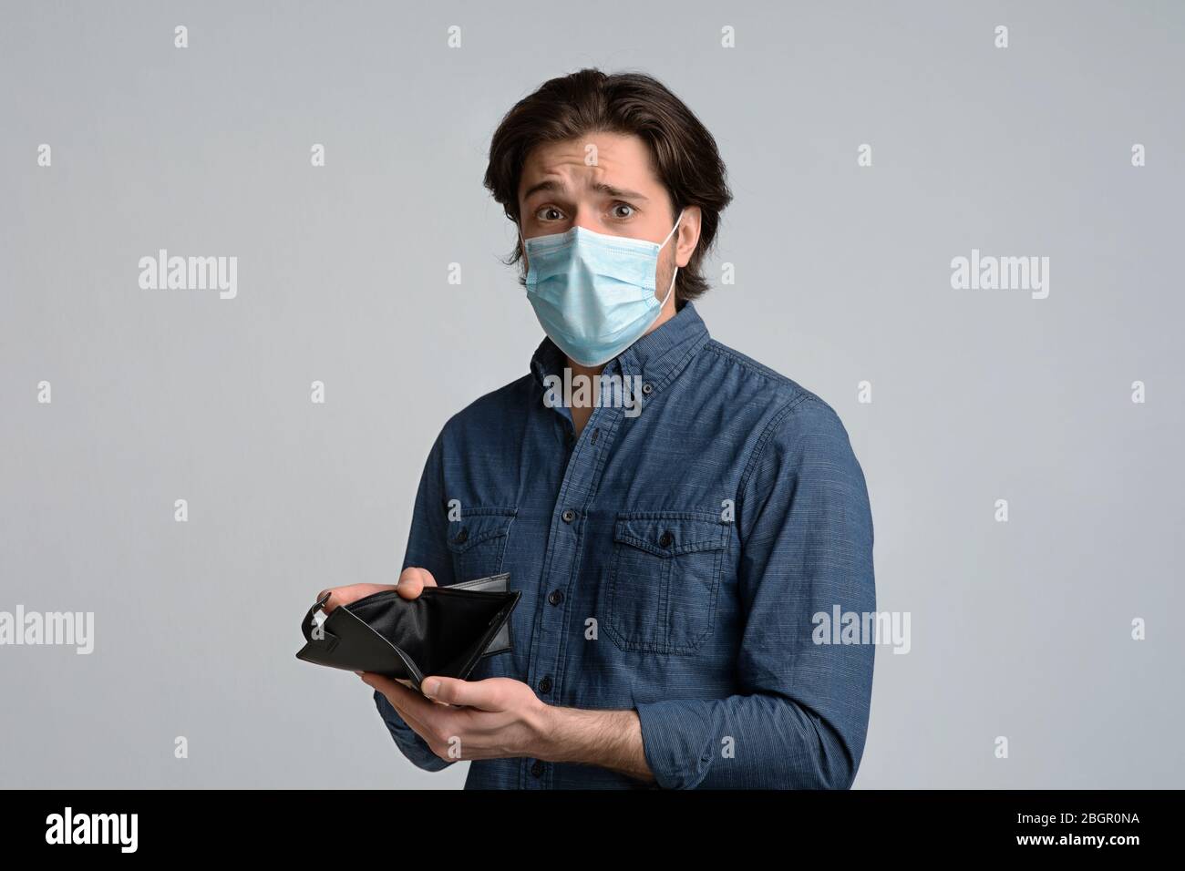 Coronavirus Economic Crisis. Worry Guy In Medical Mask Showing Empty Wallet Stock Photo