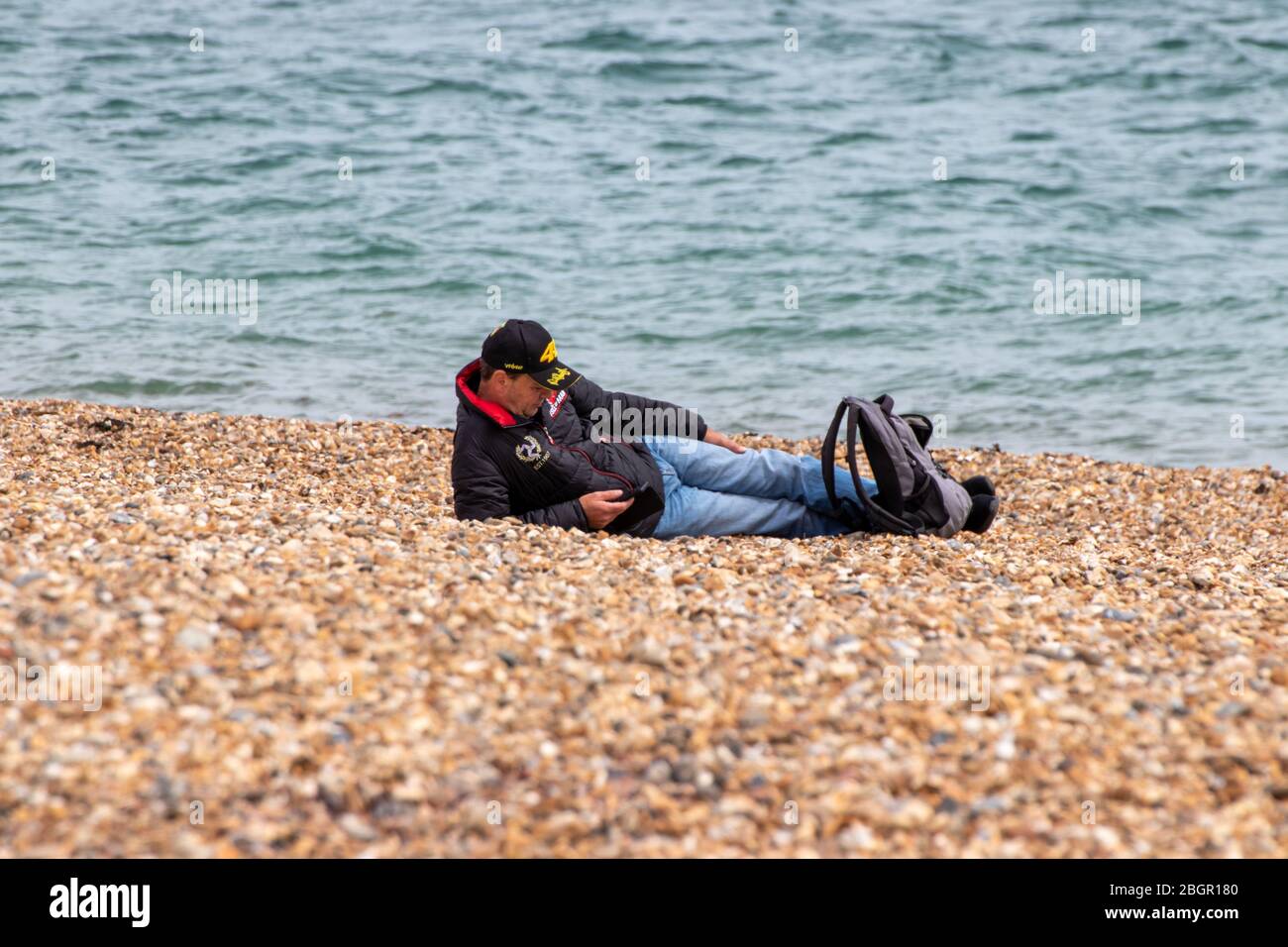 A middle aged man laying alone on a pebble beach in spring Stock Photo