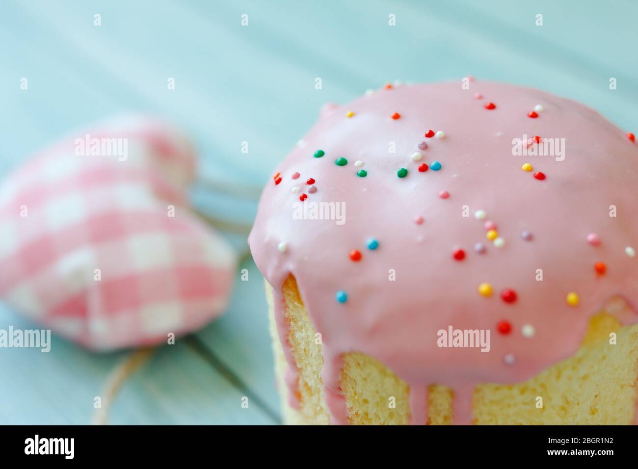 Sweet bread traditional easter orthodox celebration cake panettone also called kulich glazed with pink icing and raisins and three colored hearts on Stock Photo