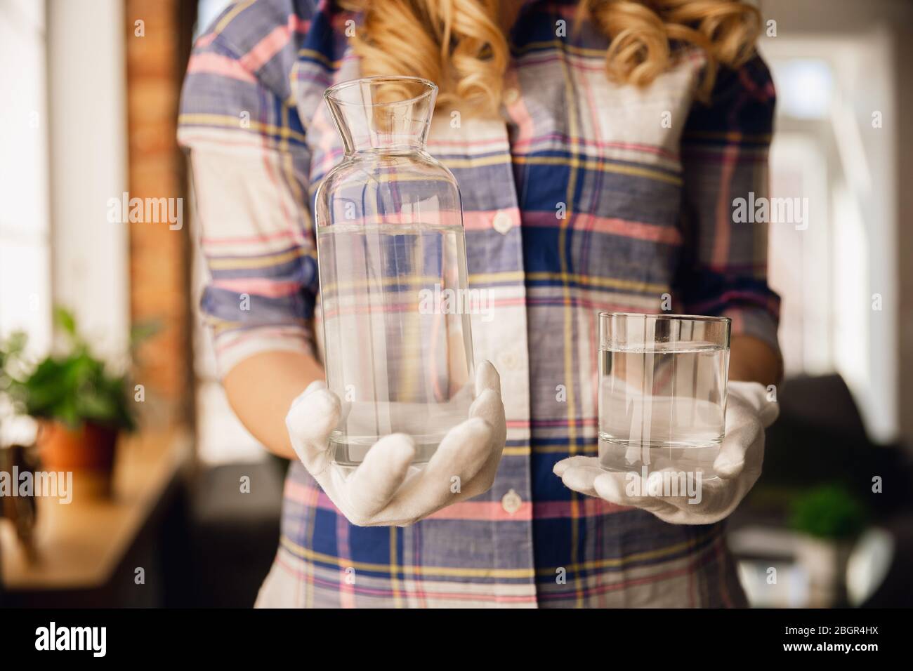 Close up of female hands in gloves holding bottle and glass with pure water. Healthy lifestyle, health care, diet. Preparing, proposing for somebody. Copyspace. Water purification, safety. Stock Photo