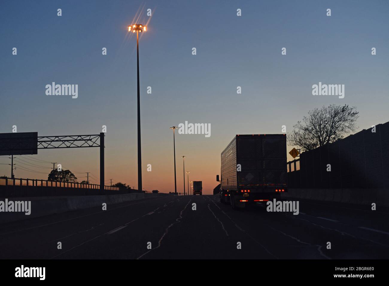 Semi trailer trucks make their way down a highway towards a sunset at dusk in southern Ontario, Canada Stock Photo