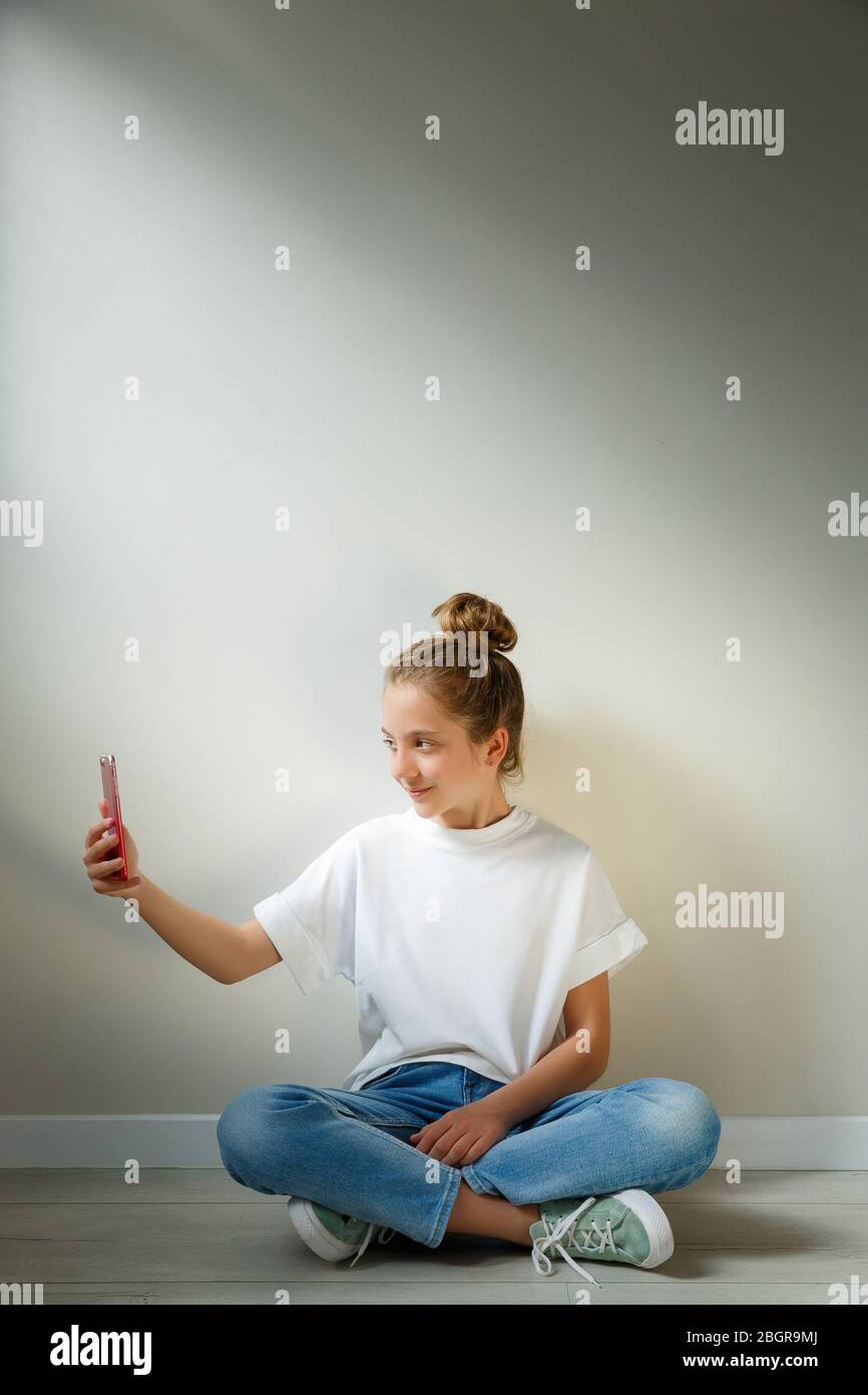 Portrait of happy young american teenager using mobile phone while sitting on a floor with legs crossed isolated over white background Stock Photo