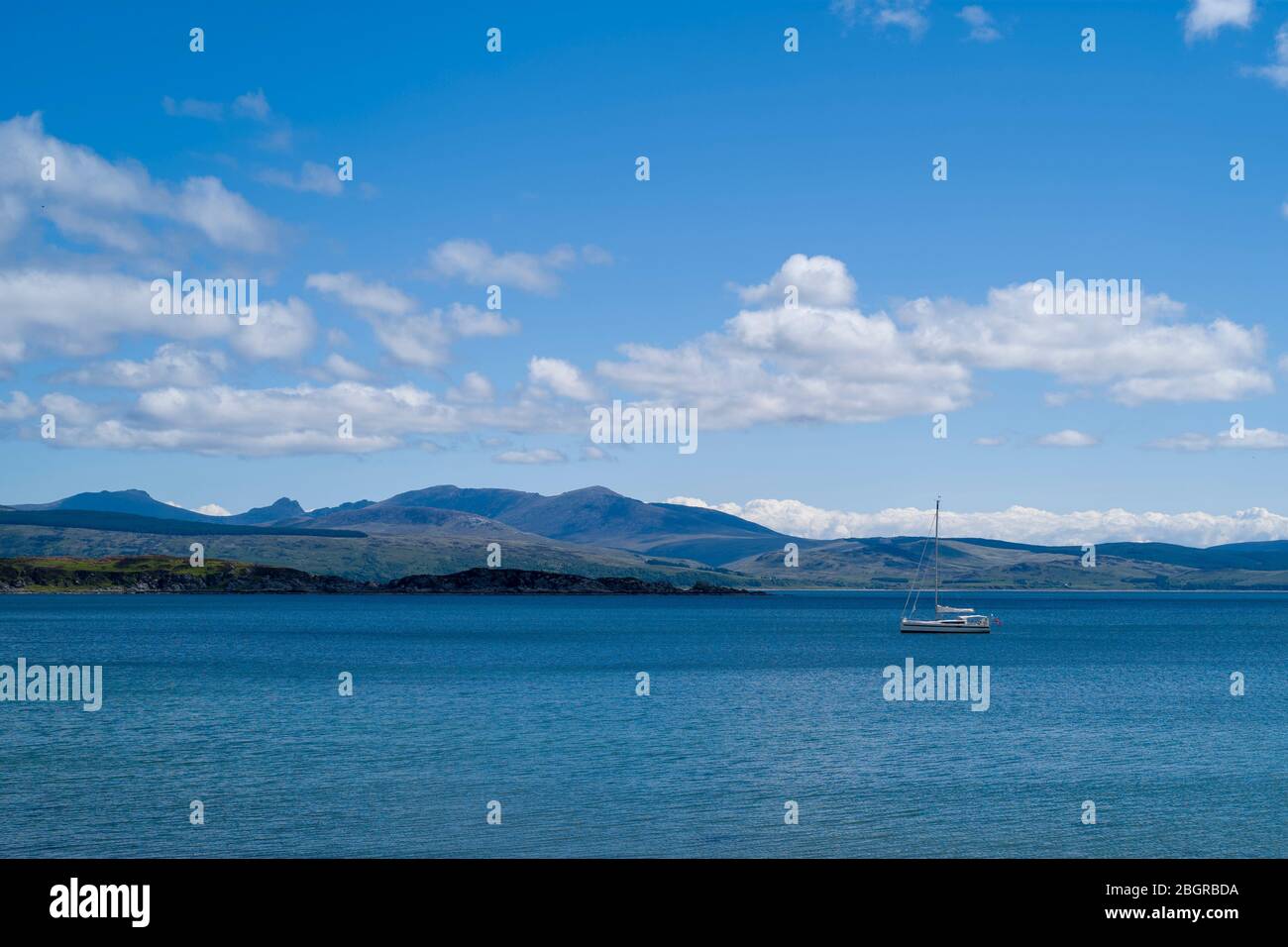 Moored yacht with Isle of Arran in distance viewed from Kintyre, Argyll coast, Scotland Stock Photo
