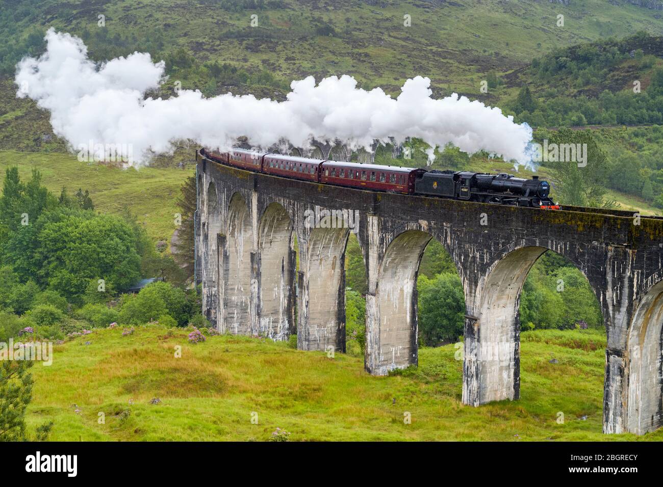 'The Jacobite' locomotive steam train on West Highland Rail crosses famous Glenfinnan Viaduct tourist spot in the Highlands of Scotland Stock Photo