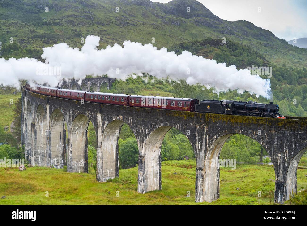 'The Jacobite' locomotive steam train on West Highland Rail crosses famous Glenfinnan Viaduct tourist spot in the Highlands of Scotland Stock Photo