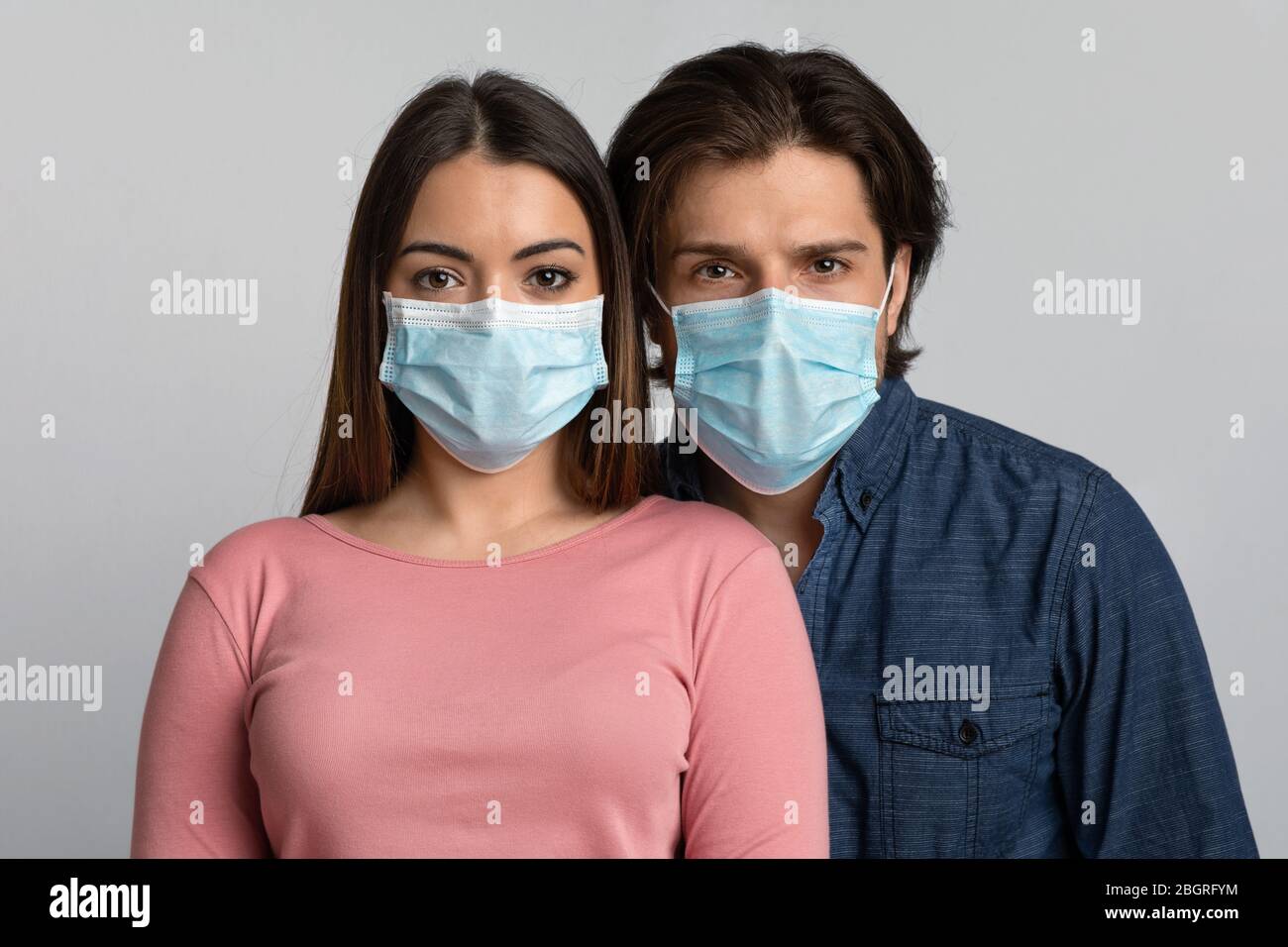 Portrait of young man and woman wearing medical masks looking at camera ...