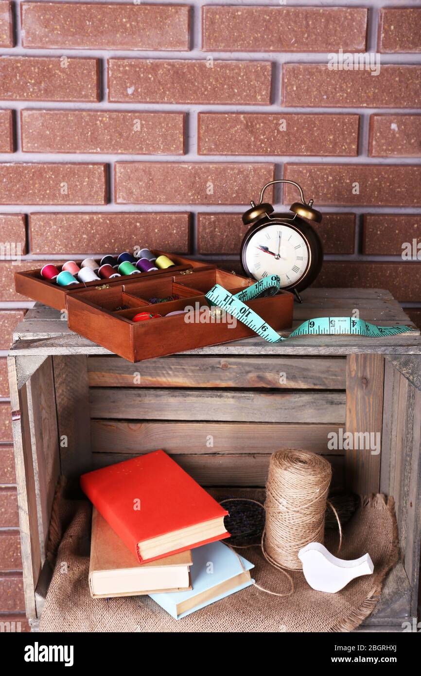 Sewing kit with tapeline, books, rope and toy bird on a wooden box in front of brick wall Stock Photo
