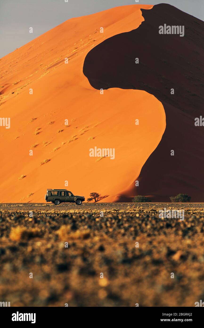 A Land Cruiser passing in front of a giant dune in Sossusvlei, Namib-Naukluft Park, Namibia. Stock Photo