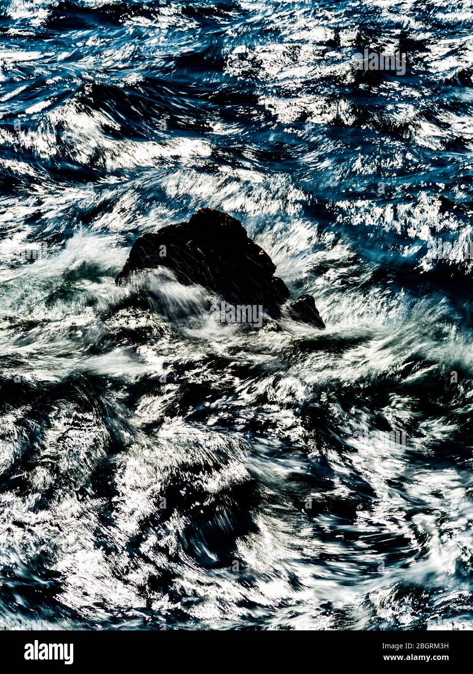 Waves crashing striking shore boulder solitary big rock intentionally slightly blurry conveying motion speed underwater dangerous for navigation Stock Photo