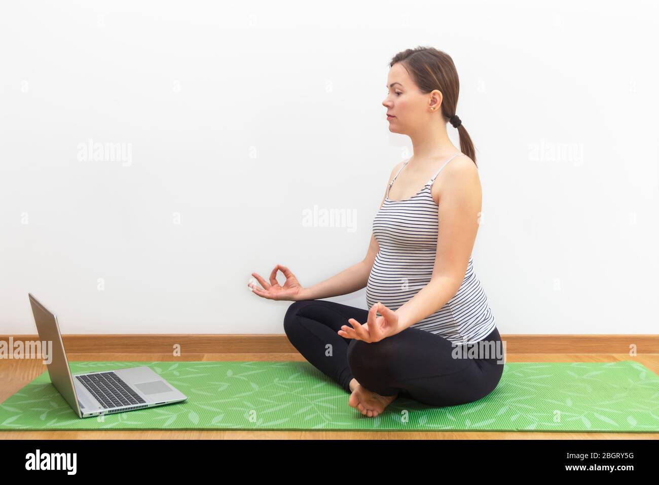 Pregnancy yoga at home during home quarantine, self-quarantine concept. Young pregnant woman practicing yoga online at home with notebook Stock Photo