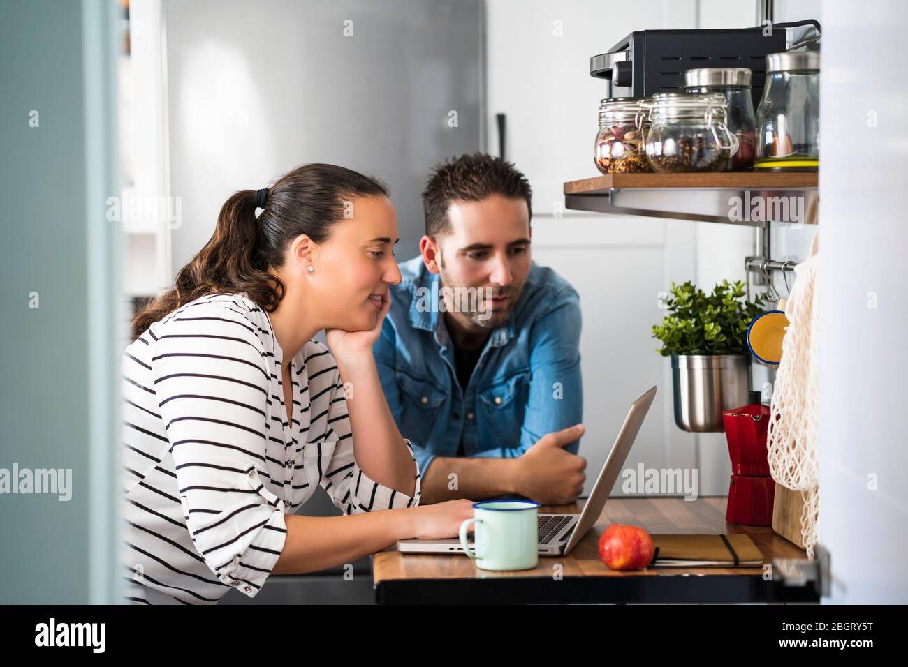 Young couple of man and woman using their laptop in the kitchen of their apartment. Work at home and stay home safely Stock Photo