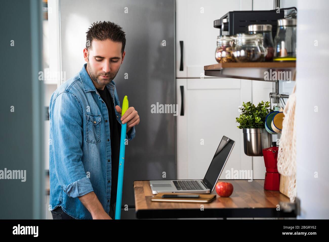 Modern Man with broom sweeping floor in his kitchen at home. Man doing tasks normally done by women. Cleaning, housework and housekeeping concept Stock Photo