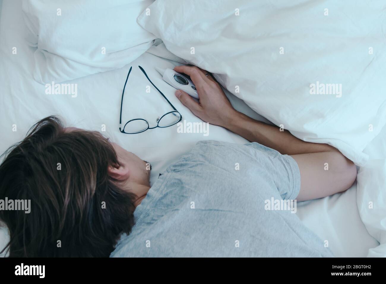 Sick young man sleeps in bed with glasses and thermometer beside him on