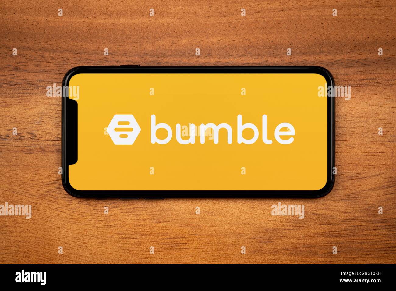 A smartphone showing the Bumble logo rests on a plain wooden table (Editorial use only). Stock Photo