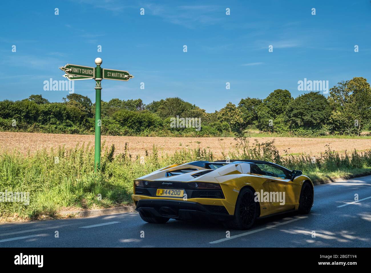Yellow Lamborghini sports car, Jersey registered number plate, driving past signpost St Martins and Trinity Church in Jersey, Channel Isles Stock Photo