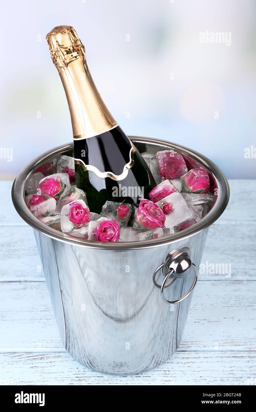 Frozen rose flowers in ice cubes and champagne bottle in bucket, on light  background Stock Photo - Alamy