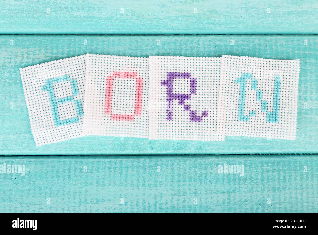 Word made embroidered letters on white fabric, on wooden background