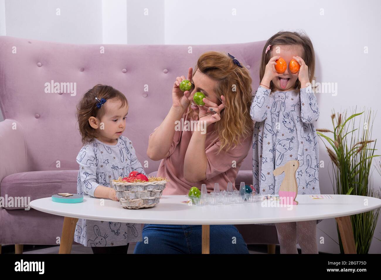 Mother and daughters are painting eggs. Happy family are preparing for Easter. Quarantine at home. Stock Photo