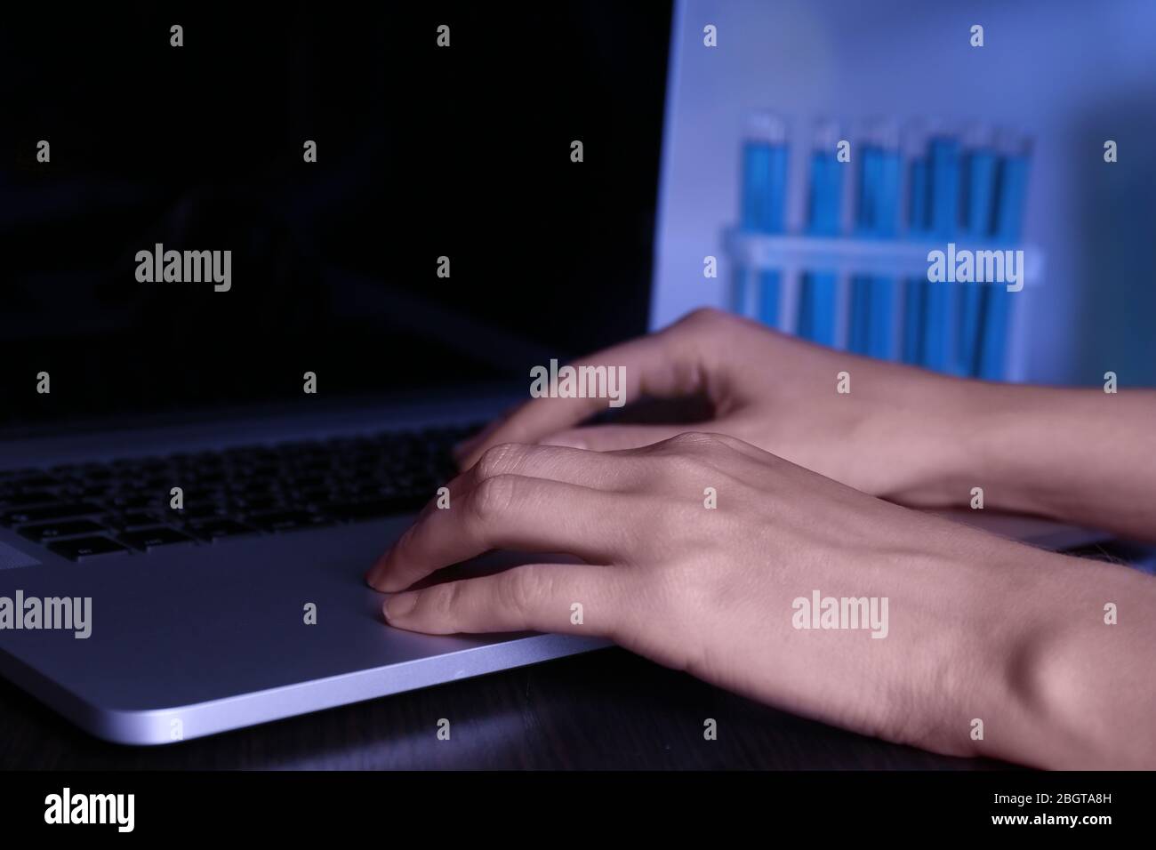 Scientist entering data on laptop computer with test tubes in a ...