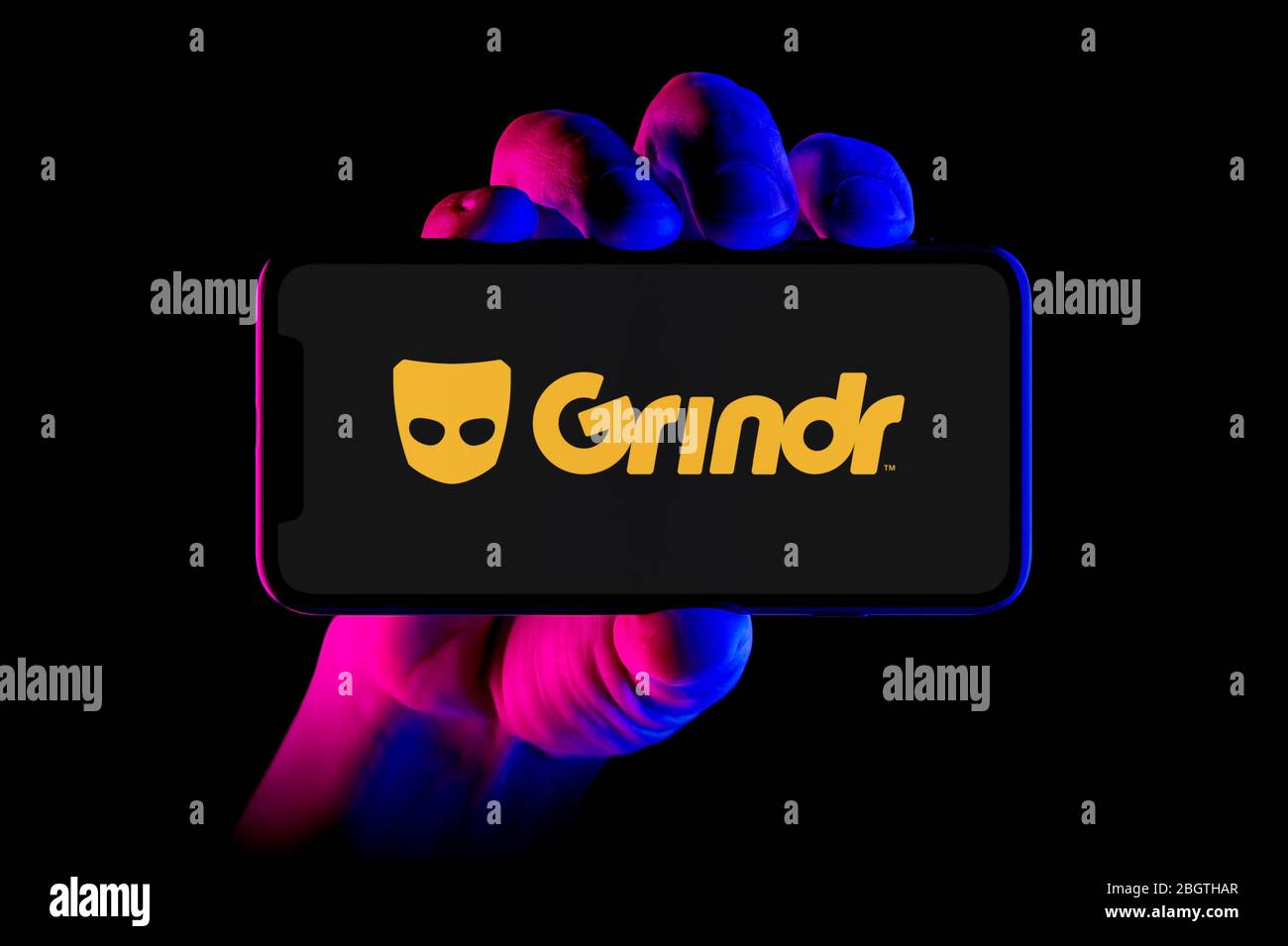 A smartphone displaying the Grindr logo is held by a hand shot on a
