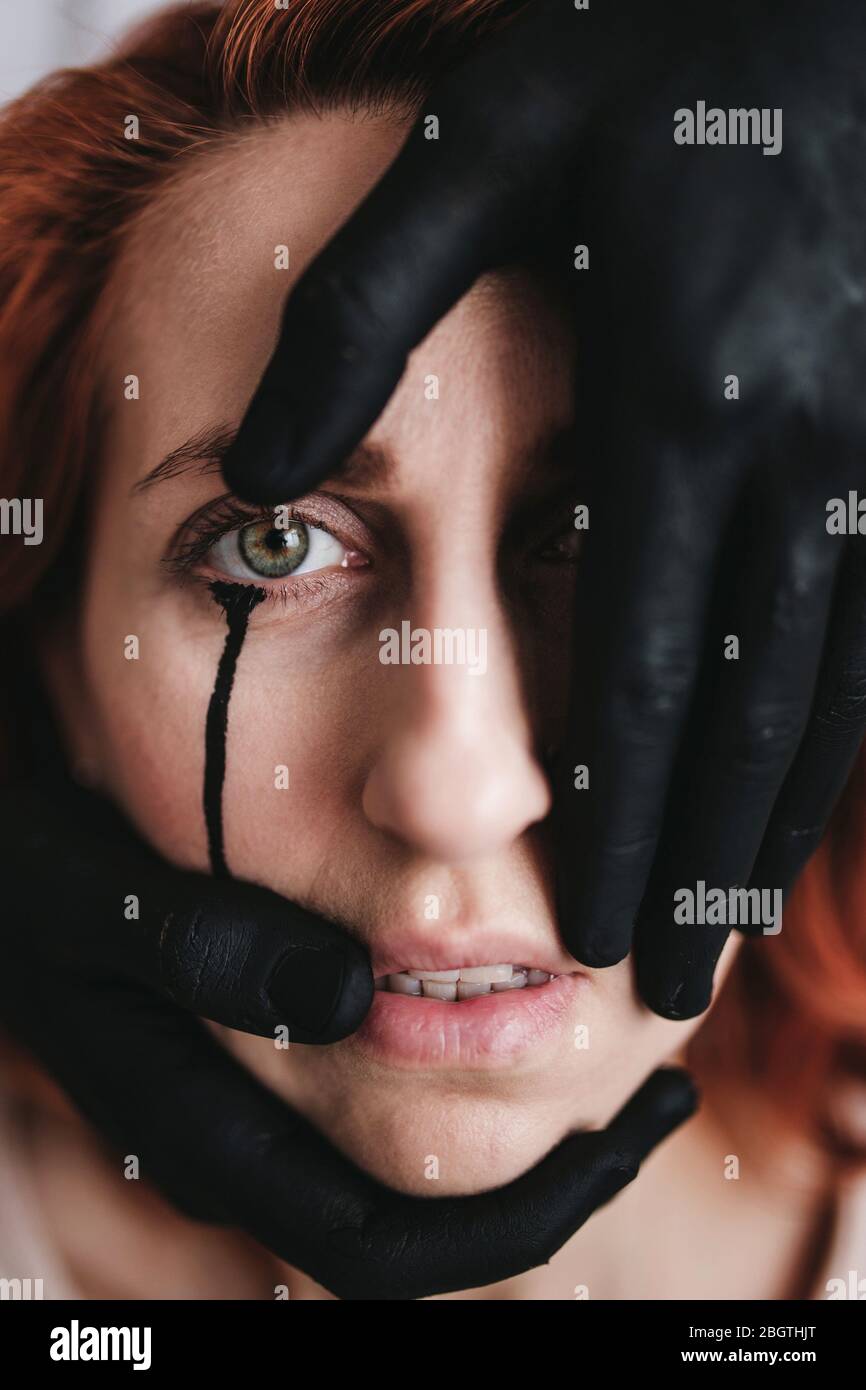 Beautiful girl with creative makeup in Gothic style. With a black tear running down his cheek. Captive outfit with two black colored hands. Stock Photo